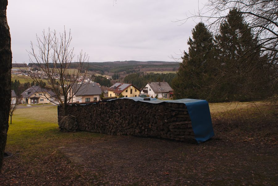 View of Neuhütten from a path to the Dollberg with a pile of wood in the foreground